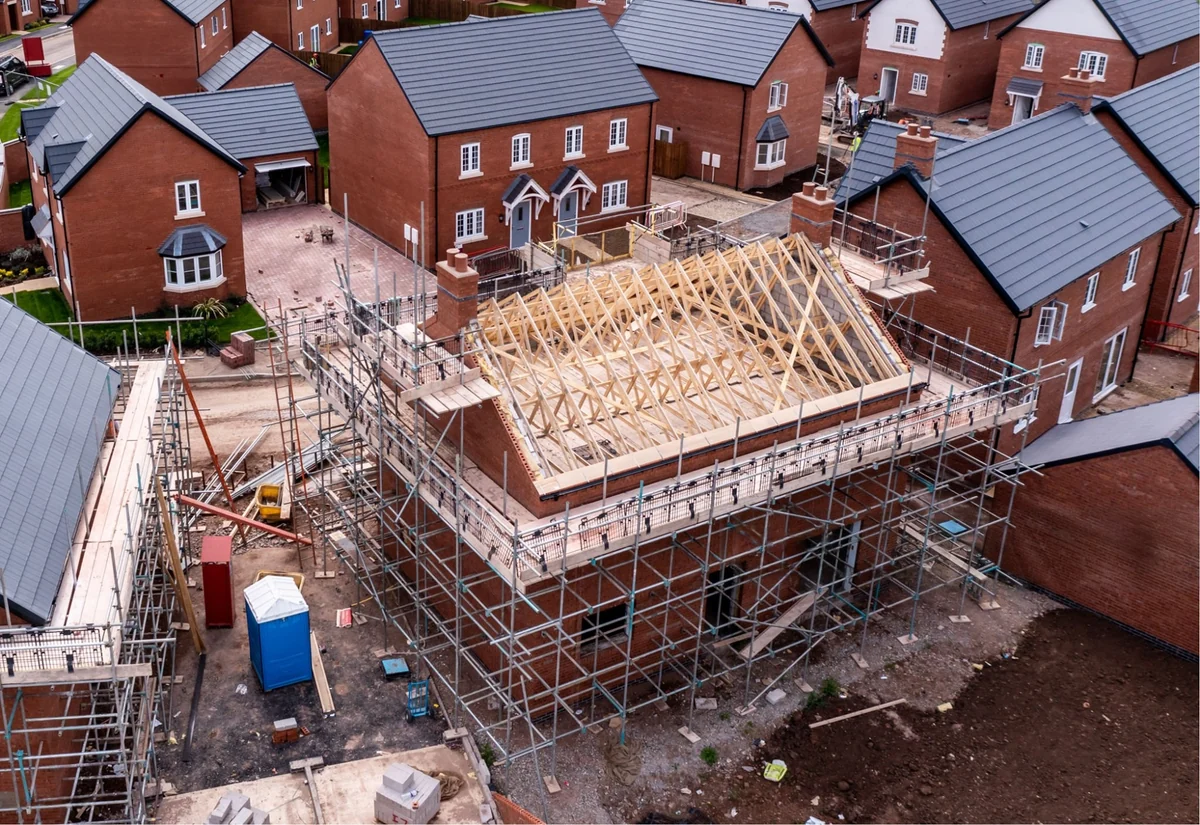 Brick houses under construction with scaffolding, exposed roof trusses and site access routes.